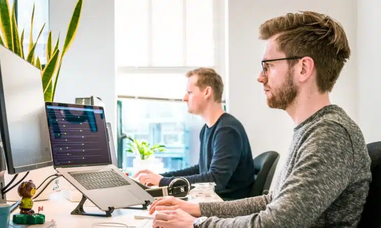 man sitting on chair wearing gray crew-neck long-sleeved shirt using Apple Magic Keyboard