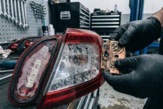 Feu arrière de berline moderne démonté sur un établi de garage, montrant des circuits LED défaillants et de la condensation à l'intérieur du boîtier